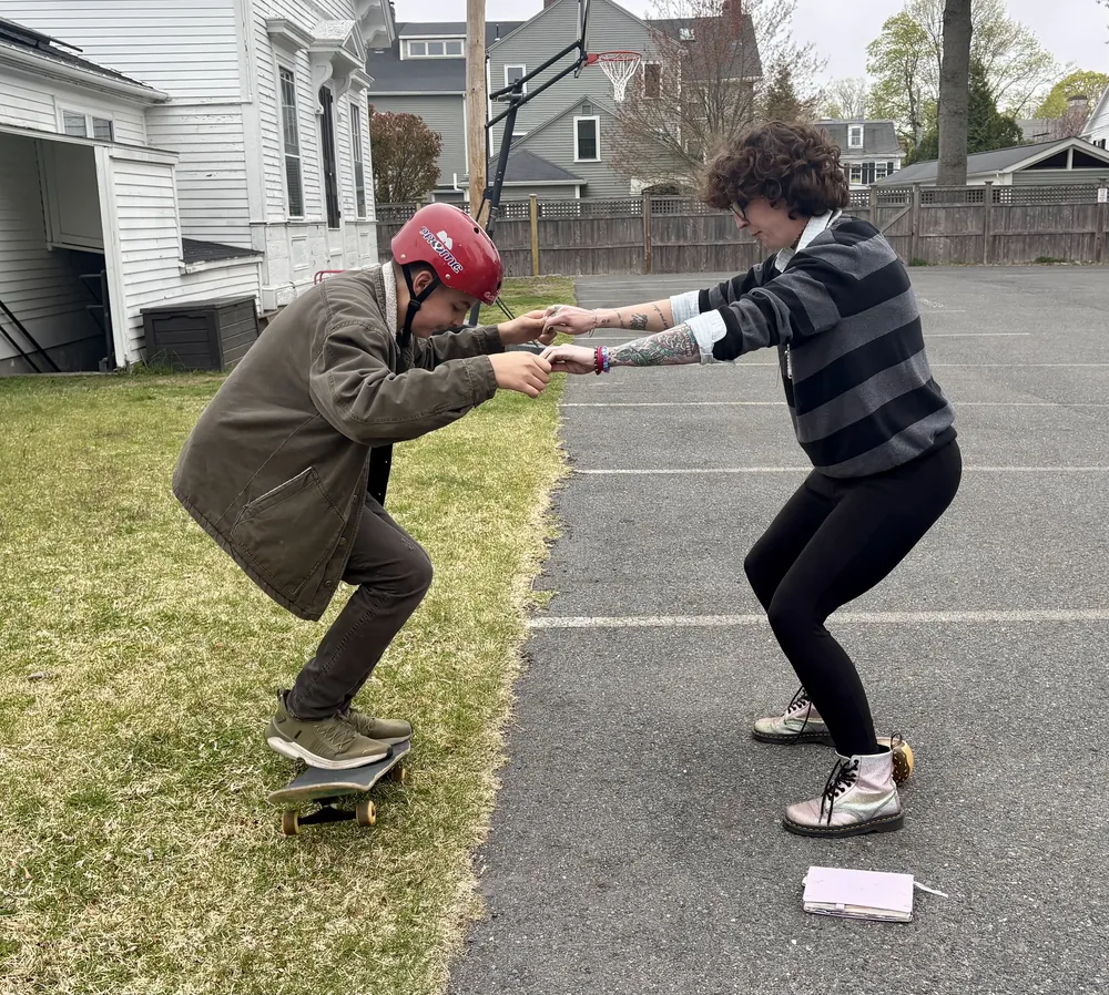 A staff member helps a BSLC member learn how to skateboard.